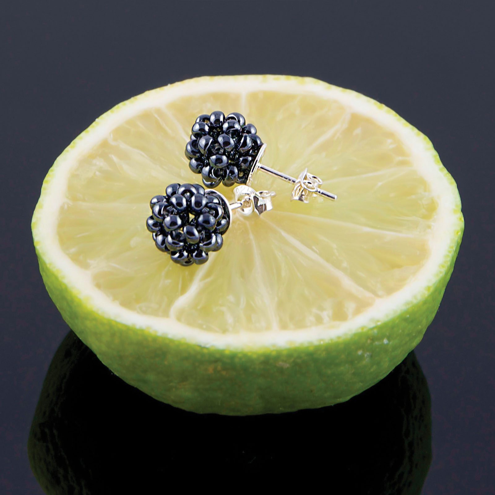 Grofova Design Earrings shaped like small dark berries placed on a sliced citrus fruit.
