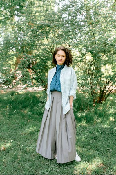 Woman in a long grey skirt and blue top standing in a garden.