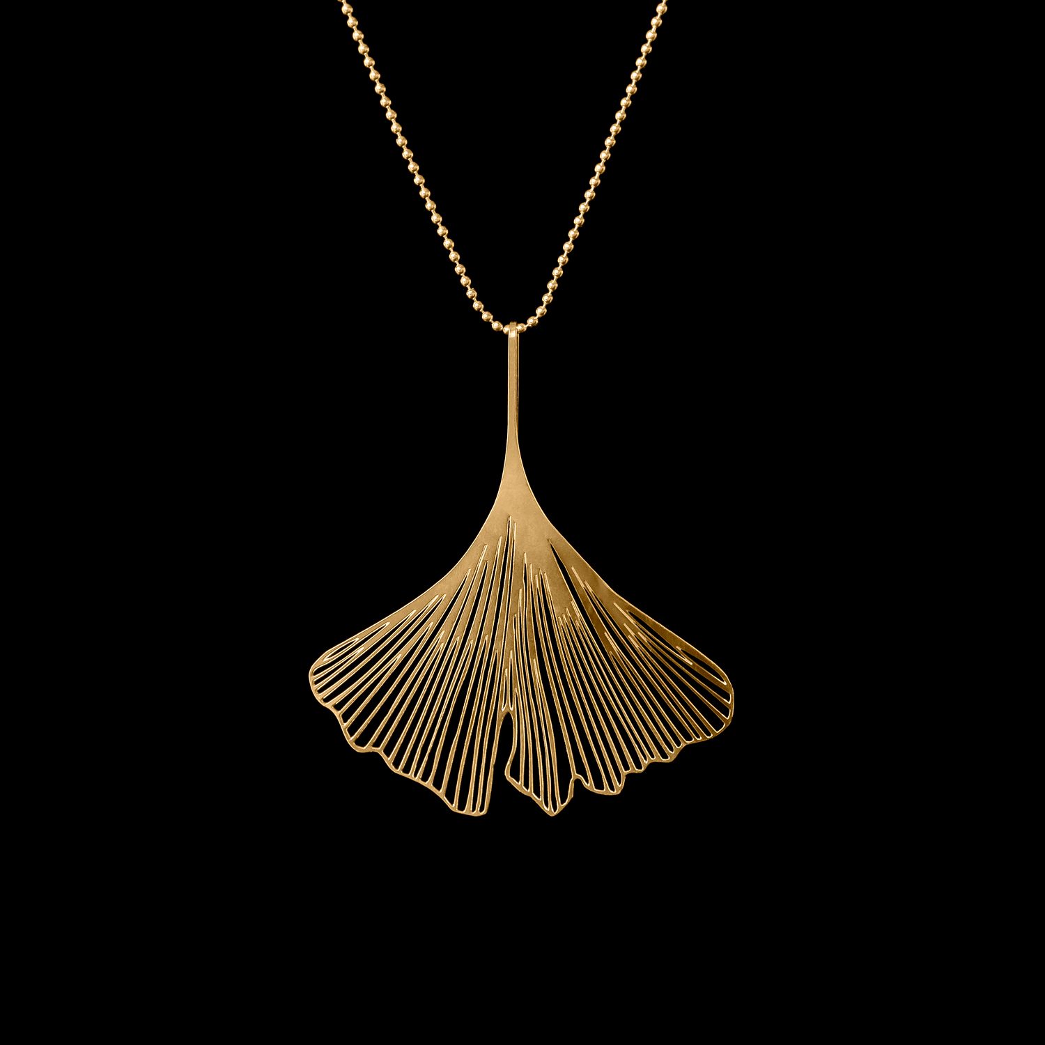 Gold necklace with a leaf-shaped pendant against a black background.