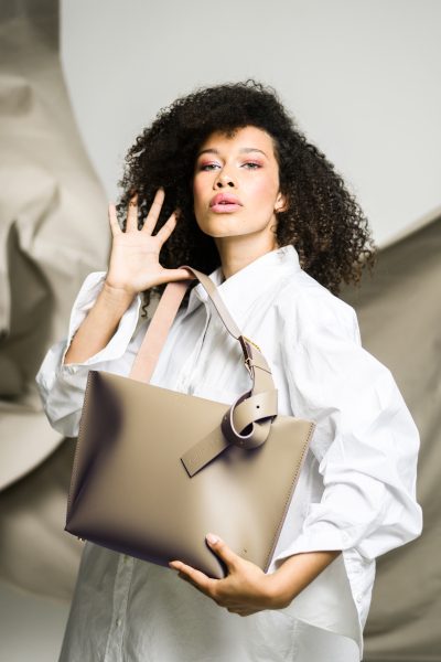 Woman in a white shirt holding a large beige handbag.