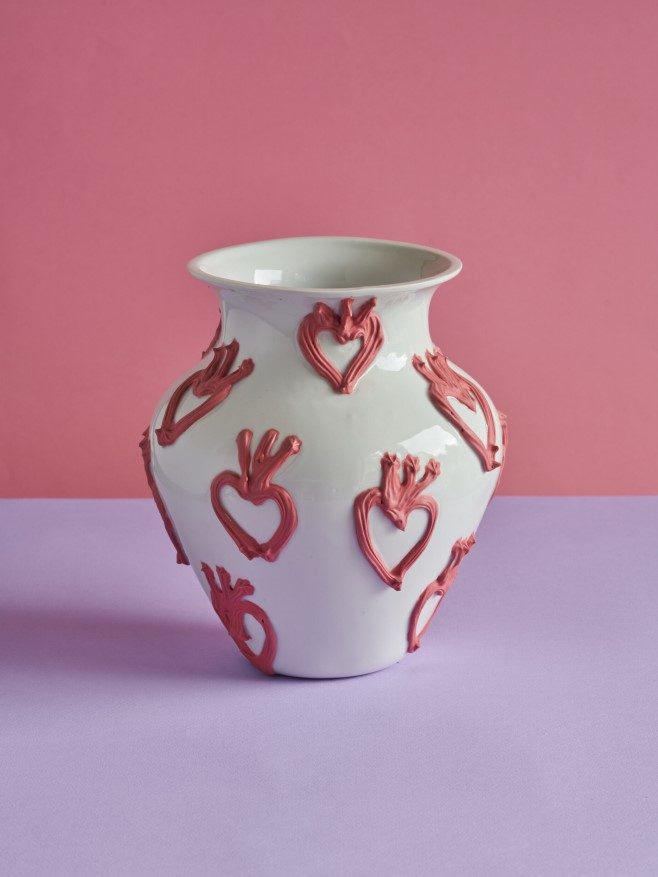 Pale ceramic vase with raised pink motifs against a pink background.