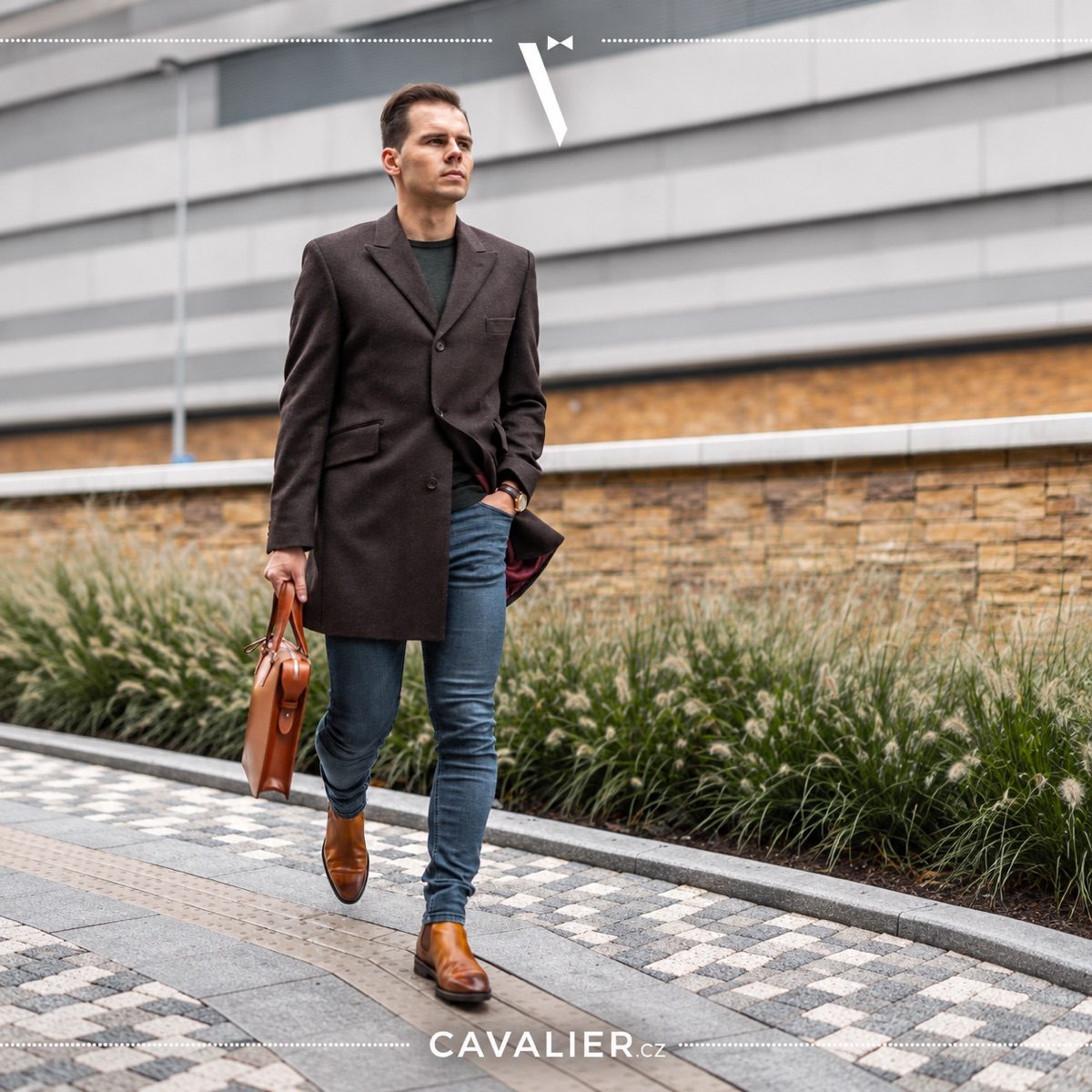 Man in a brown coat, jeans and brown shoes carrying a leather bag.