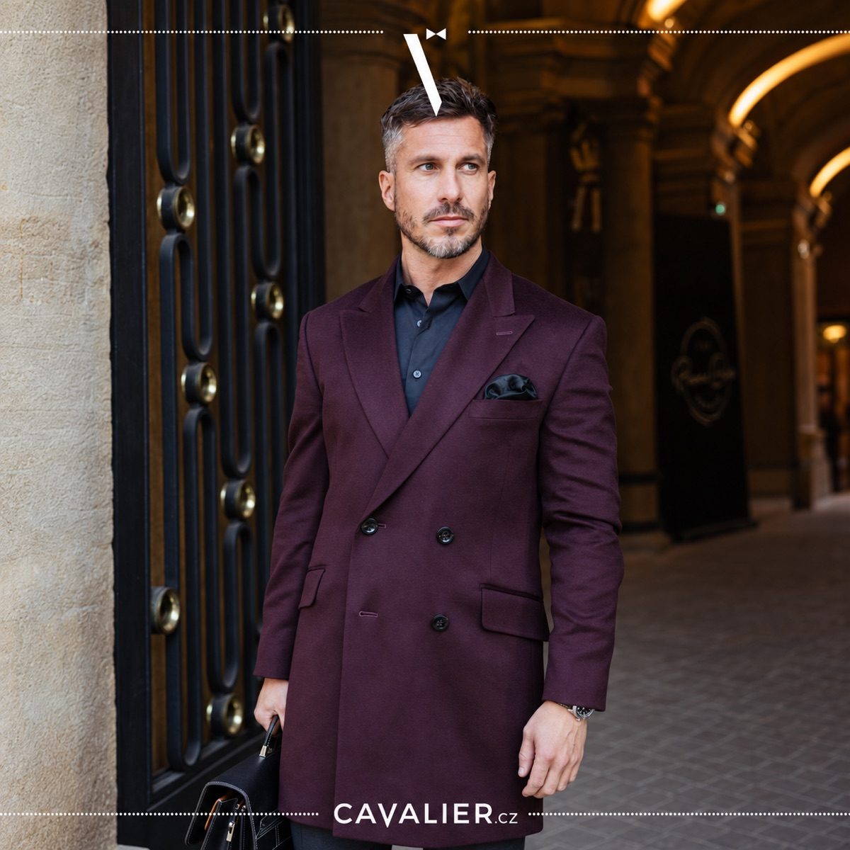 Man wearing a burgundy double-breasted Cavalier coat with a black shirt and leather briefcase.