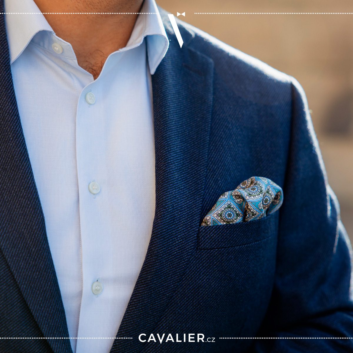 Close-up of a textured navy blazer, light blue shirt and blue patterned pocket square.