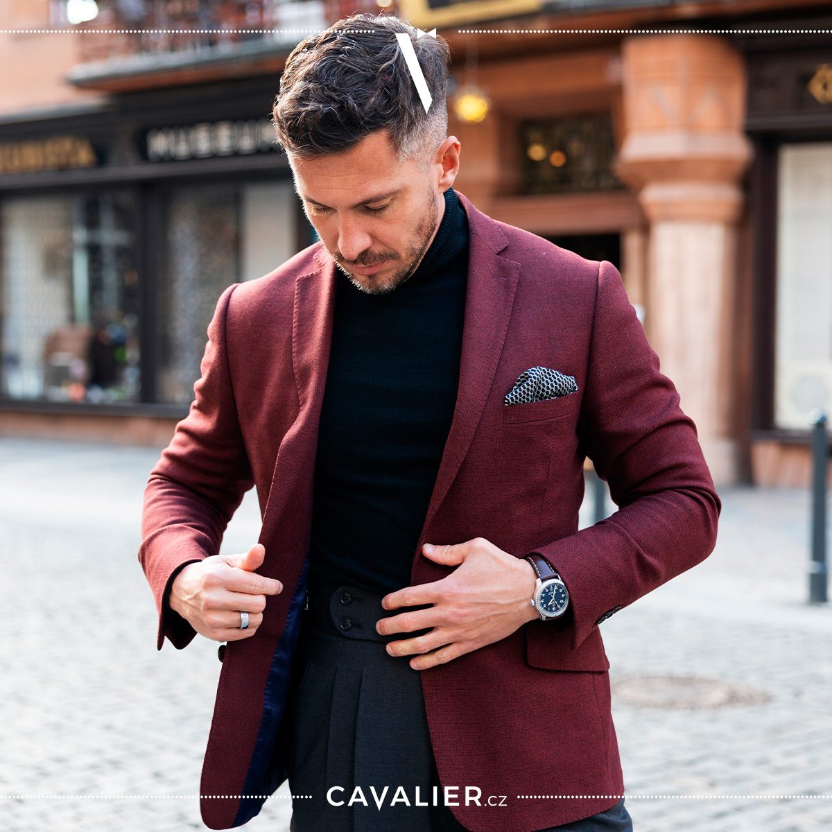 Man in a burgundy blazer, black roll-neck and patterned pocket square.