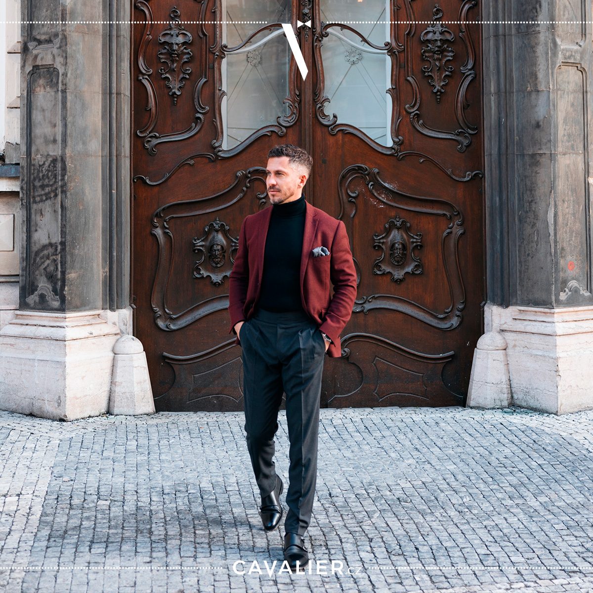 A man in a burgundy Cavalier made-to-measure wool jacket with a black roll-neck, dark pleated trousers and leather shoes