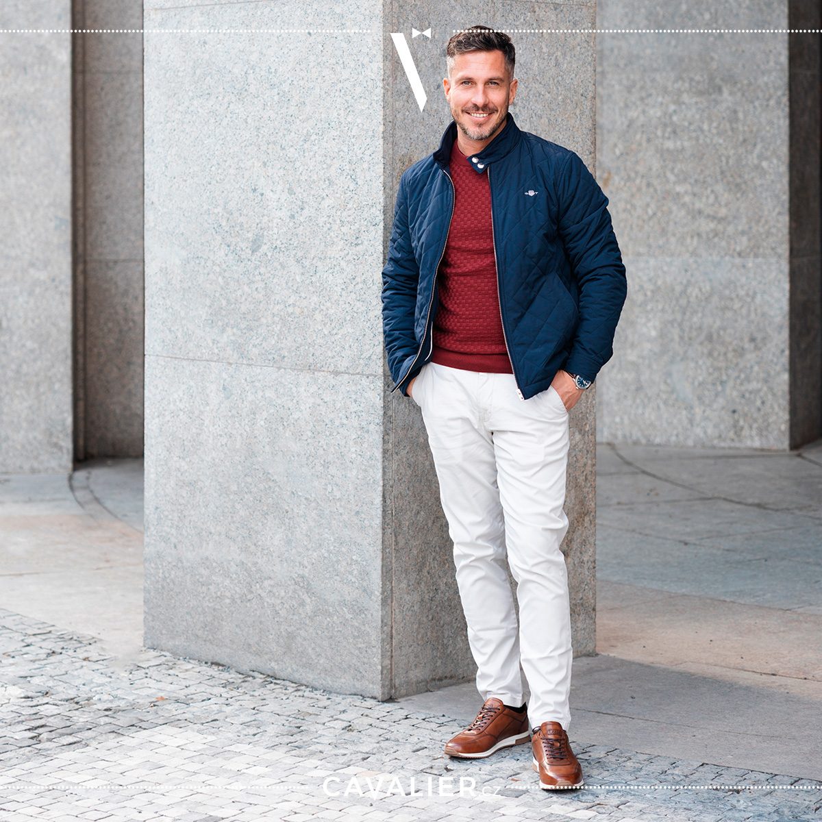 A smiling man in a navy quilted jacket, burgundy knit and light Cavalier made-to-measure trousers, showing smart casual layering for cooler days