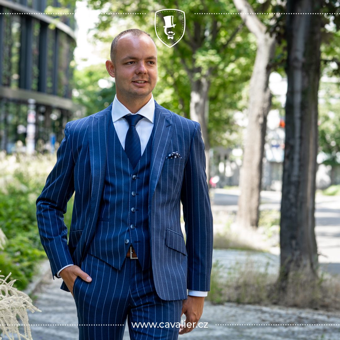 Man wearing a blue pinstripe three-piece suit with a white shirt and navy tie.