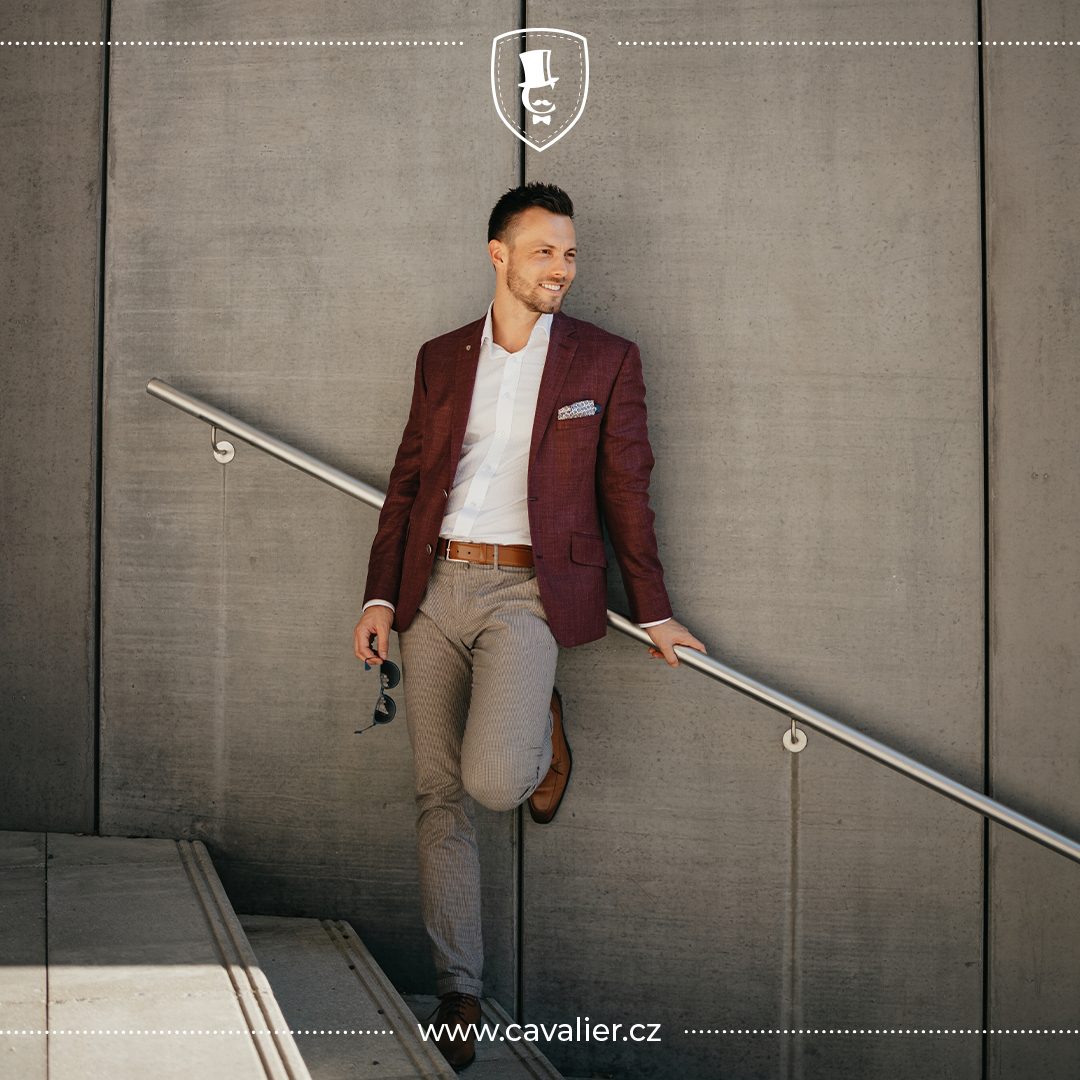 Man in a burgundy blazer, white shirt and light trousers beside a concrete stairway.