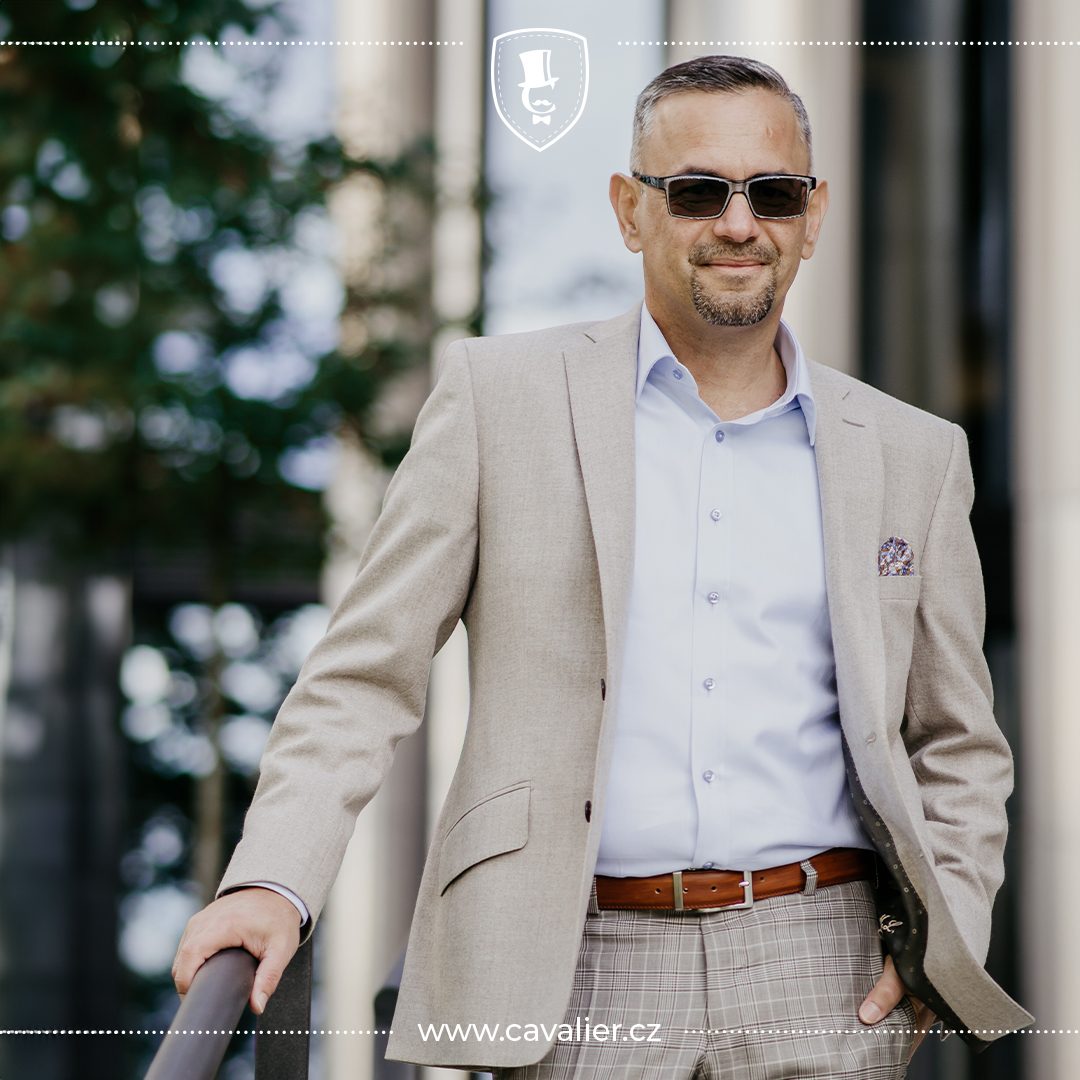Man in a light beige jacket, white shirt and sunglasses beside a railing.
