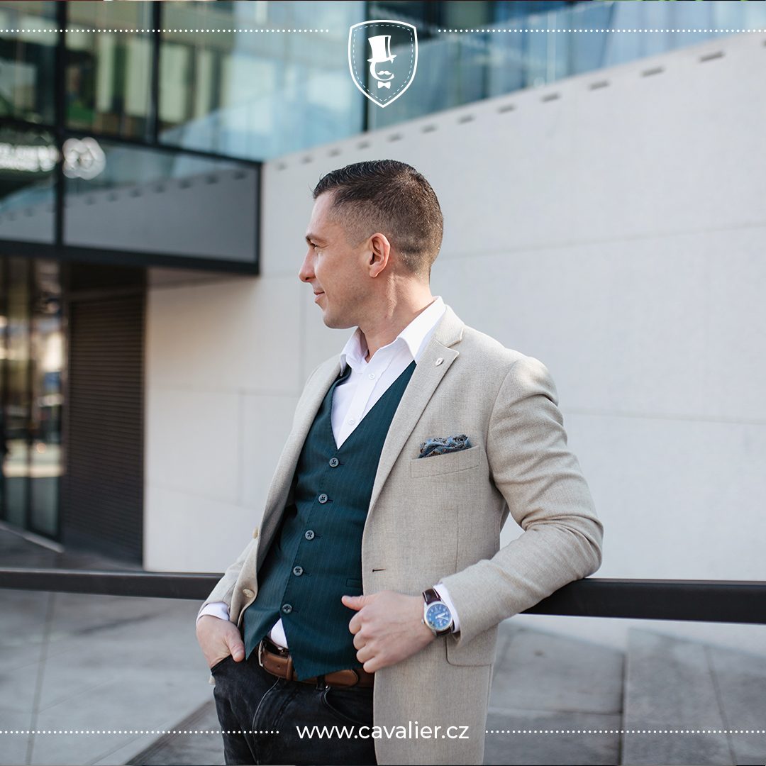 A man in a light textured Cavalier made-to-measure jacket, dark green waistcoat and open-collar white shirt with a pocket square
