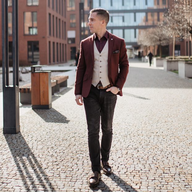 Man in a burgundy blazer and light waistcoat walking along a street.